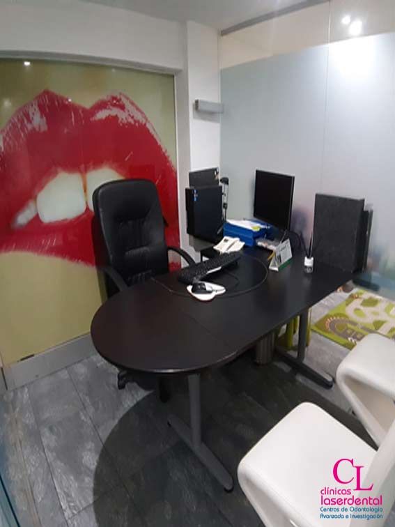 despacho 2 situado en la planta senda de la clinica dental, con su mesa, ordenador, monitor y una silla para el trajador y de fondo una foto de una boca a modo de decoracion